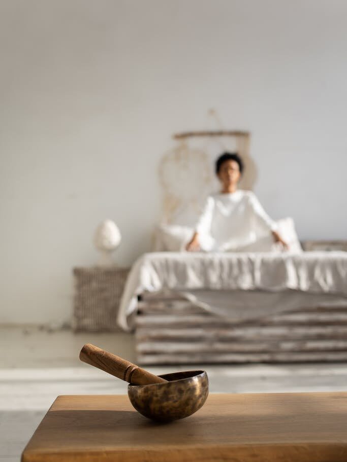 Buddhist Singing Bowl Standing on a Table and a Woman Sitting on Bed Relaxing in the Background
