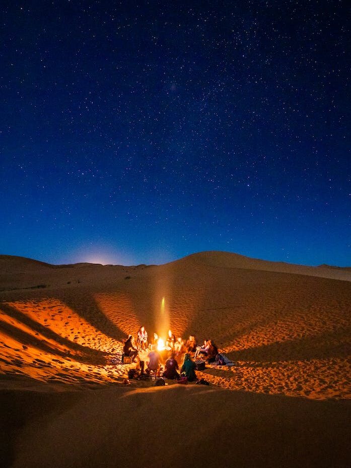 People Sitting in Front of Bonfire in Desert during Nighttime